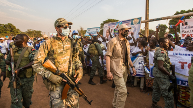 Soldiers escort a crowd holding banners at a rally.